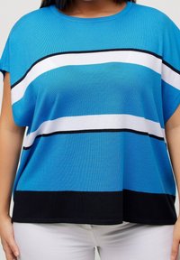 Modrá krátká tričko s krátkým rukávem, které má střídající se horizontální pruhy v bílé a černé barvě na hrudi, s volným střihem a jemnou texturou.