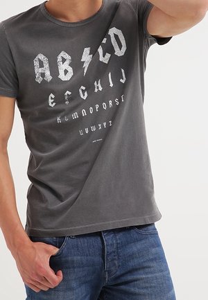 Szara bawełniana koszulka z krótkim rękawem, ozdobiona odważną, postarzającą białą grafiką alfabetu. Okrągły dekolt i luźny krój. Wykonana z miękkiego materiału.