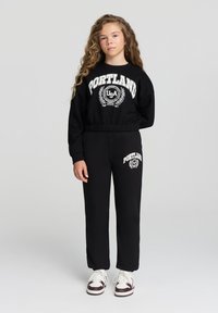 Completo felpa nera e pantaloni con grafica "PORTLAND USA". Tessuto morbido e testurizzato con polsini e vita a coste. Accenti bianchi.