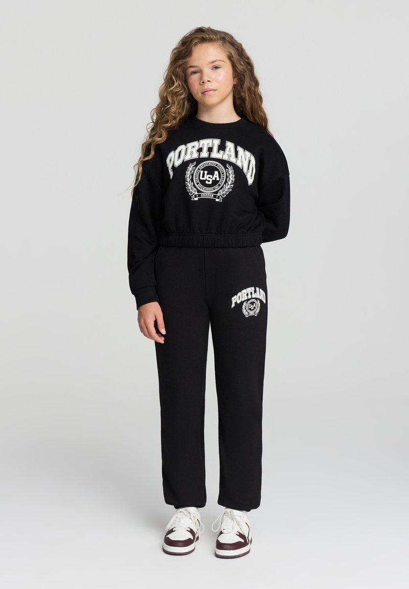 Completo felpa nera e pantaloni con grafica "PORTLAND USA". Tessuto morbido e testurizzato con polsini e vita a coste. Accenti bianchi.