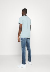 Jasnoniebieska bawełniana koszulka z krótkimi rękawami, w połączeniu z jasnoniebieskimi dopasowanymi jeansami. Model widoczny od tyłu, w białych trampkach.