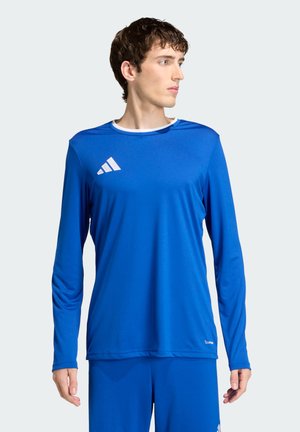 Ung mand iført en blå langærmet sportstop og matchende bukser, der kigger til venstre mod en ensfarvet baggrund.