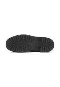 Black rubber shoe sole with deep tread pattern and textured surface, featuring circular and elongated grooves for traction.