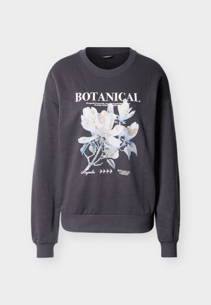 Mørkegrå genser med blomstrete magnolia-grafikk og teksten "BOTANICAL" og "BOTANICAL GARDEN" på forsiden.