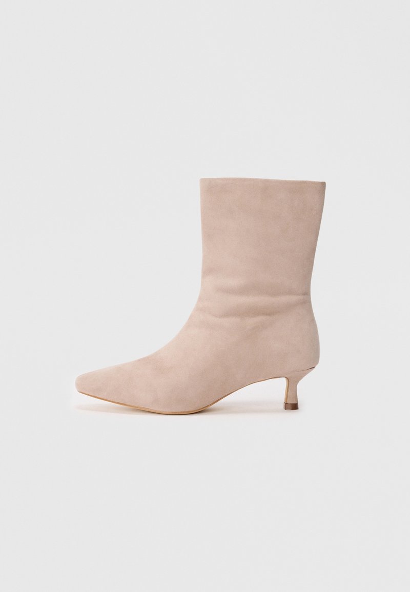 Botte mi-mollet en daim beige avec bout pointu et petit talon kitten, vue de côté sur un fond gris clair uni.