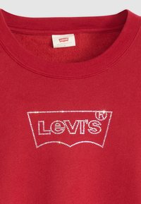 Červená mikina, bavlněný materiál, s bílým logem Levi's zdobeným krystaly. Klasický kulatý výstřih, jemná textura a tradiční design.