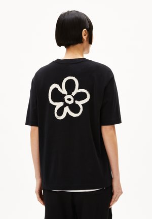 Zwarte katoenen T-shirt met een grote witte bloemenafbeelding op de achterkant. Korte mouwen, ontspannen pasvorm, minimalistisch ontwerp en klassieke ronde hals.