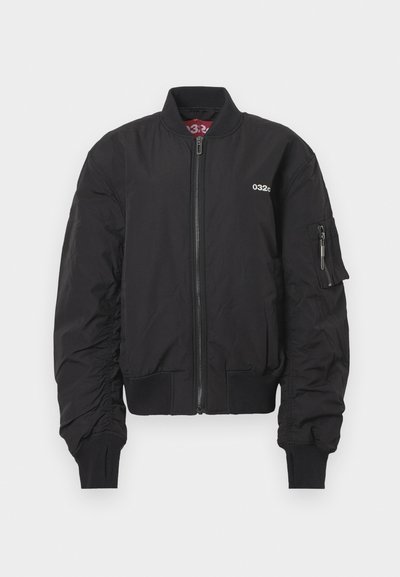 Černá bomber bunda s předním zipem, žebrovaným límcem a manžetami, malým bílým logem "032c" na hrudi a kapsou na zip na levém rukávu.