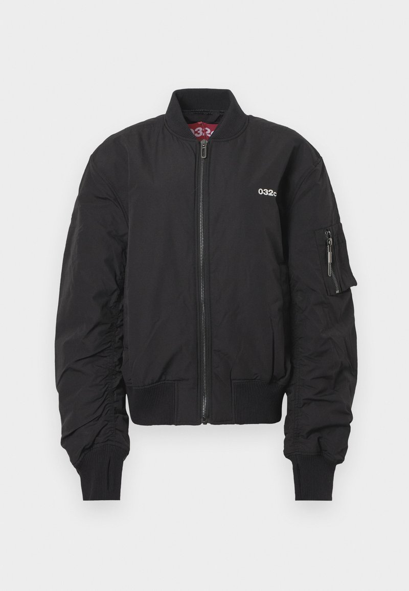 Black bomber jacket with front zipper, ribbed collar and cuffs, small white "032c" logo on chest, and zippered pocket on left sleeve.