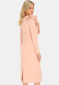 Dopasowana różowa sukienka z długimi rękawami, falbaną na ramieniu i rozporkiem z tyłu. Gładki materiał o dopasowanej sylwetce.