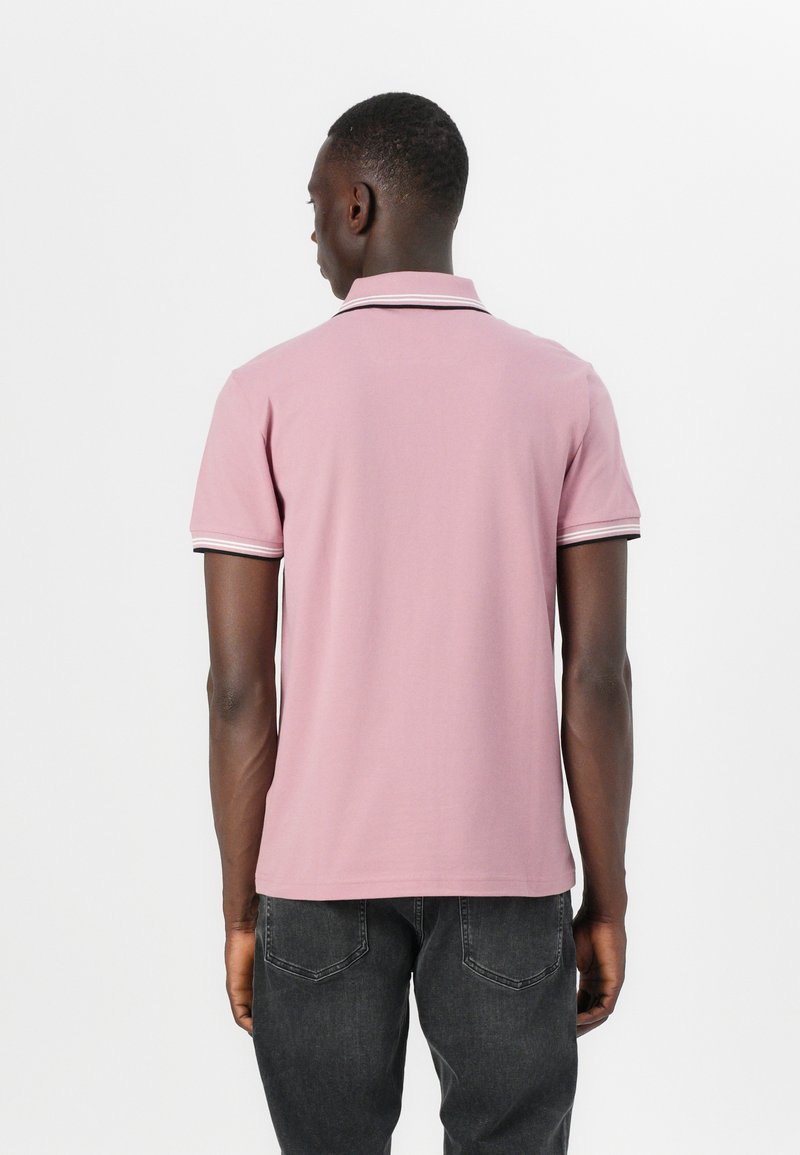 Polo en algodón de color rosa claro con un ribete negro en el cuello y las mangas. Mangas cortas, diseño ajustado.