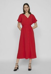 Czerwona sukienka do kolan z dekoltem w kształcie litery V, krótkimi rękawami i zapięciem na guziki. Posiada elastyczny pasek w talii oraz swobodny krój.