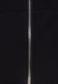 Sudadera con cremallera negra que presenta una cremallera metálica centrada, fabricada en un material de algodón suave con textura de canalé.