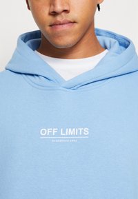 Felpa leggera blu con cappuccio realizzata in materiale morbido, caratterizzata da una stampa bianca con il slogan "OFF LIMITS DANGEROUS AREA" sul petto; include un cappuccio con cordini.