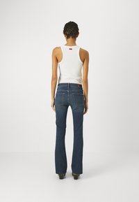 Jeans blu svasati con lavaggio medio, tasche posteriori e dettaglio del logo rosso del marchio. Abbinati a un top senza maniche bianco.