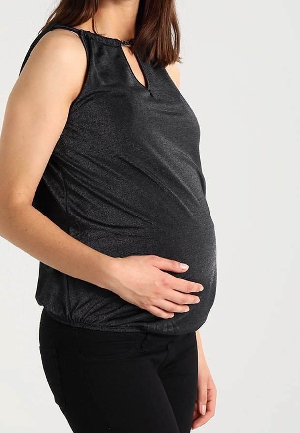 Svart ärmlös gravidblus med en glänsande yta, nyckelhålsutskärning och draperad nederkant, bärs över svarta byxor.