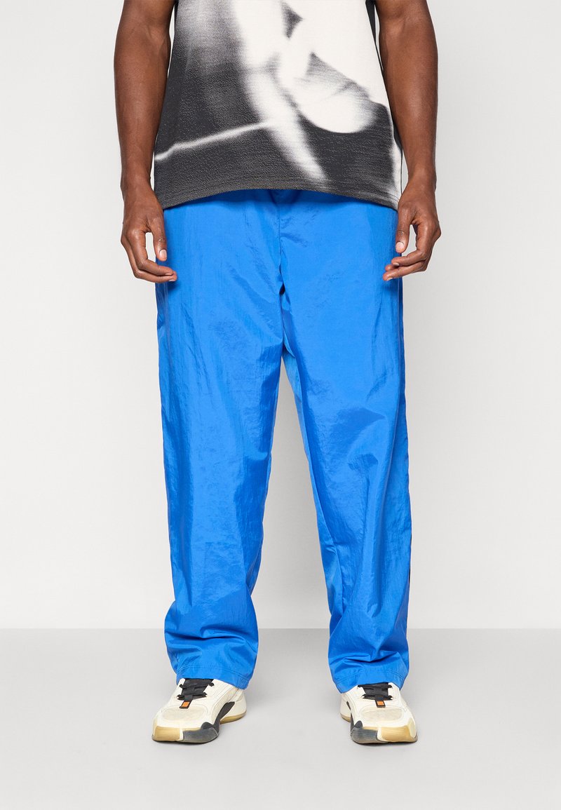 Blauwe nylon broek met een relaxed fit, voorzien van een zachte textuur en een elastische tailleband. Gecombineerd met wit- en zwartkleurige sneakers.