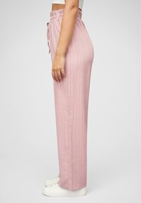 Pantalons larges rose texturé avec une taille smockée et un cordon de serrage. Associés à des baskets blanches, montrant une vue de côté du design.