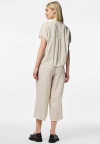 Conjunto de dos piezas a rayas en color beige, con blusa de manga corta y pantalones cortos. Textura suave. Detalle de pliegue en la parte posterior de la blusa. Zapatos negros planos.