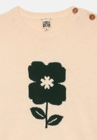 Maglione beige lavorato a maglia con un grande motivo a fiore verde scuro, con una forma interna bianca e foglie verdi, decorato con due bottoni marroni sulla spalla.