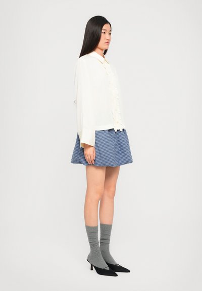 Valge nööpidega särk volangidega, millele on lisatud sinine ruuduline seelik. Hallid sokid ja mustad terava ninaga kontsad lõpetavad komplekti.