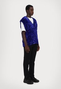 Mėlynas blizgučiais puoštas bevandenis megztinis virš baltos marškinėlių, derinamas su juodais kelnėmis ir juodais batais. Savinasi V formos iškirptę ir tekstūruotą paviršių.