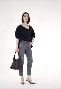 Suéter negro de gran tamaño con escote en V, jeans gris desgastados y tacones de estampado de leopardo. Bolsa tote marrón con dos asas. Fondo neutro.