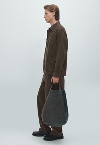 Donkerbruine corduroy knoopjack en bijpassende broek, gecombineerd met een donkergrijze leren tote bag met gestructureerde handvatten. Zwarte schoenen.