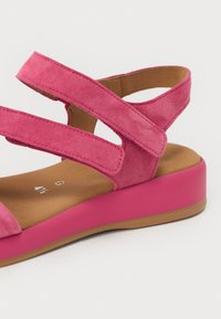 Rosa semskesandal med to brede kryssstropper, en polstret brun såle og en kraftig rosa såle. Har en glatt overflate og et komfortabelt design.