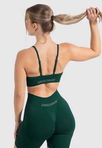 Mörkgrön träningsset bestående av en kort sport-bh med justerbara remmar och högmidjade shorts, båda med diskret branding.