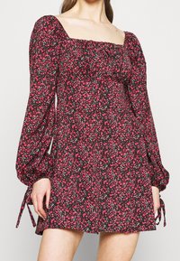 Musta kukkamekko pitkillä puff-hihoilla, jossa on neliökaula-aukko. Kuosi sisältää vaaleanpunaisia ja valkoisia kukkia. Sivusiteet hihoissa.