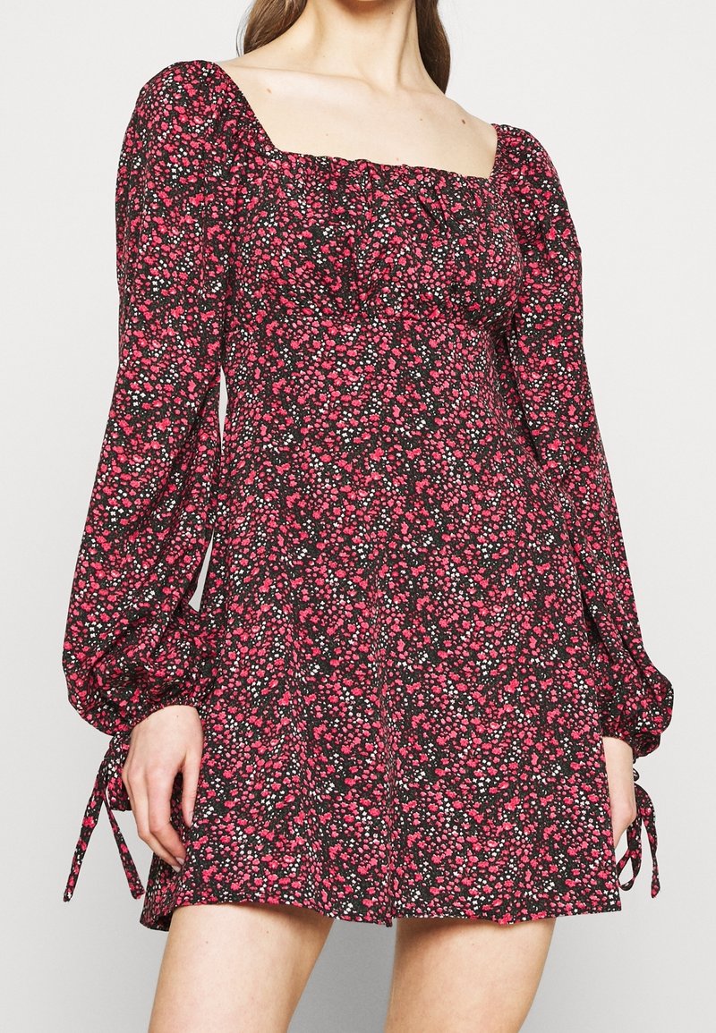 Musta kukkamekko pitkillä puff-hihoilla, jossa on neliökaula-aukko. Kuosi sisältää vaaleanpunaisia ja valkoisia kukkia. Sivusiteet hihoissa.