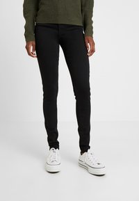 Svarta slim-fit jeans i stretchdenim med en enkel design utan synliga mönster, ihopparade med vita sneakers.
