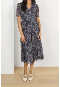 Marineblaues Blumenkleid mit kurzen Ärmeln, gestuftem Design und leichtem Stoff, versehen mit verstreuten weißen und goldenen Blumenmustern.