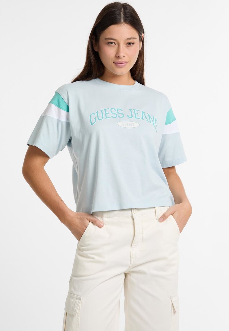 Šviesiai mėlynas, trumpas marškinėlis su užrašu "GUESS JEANS 1981" atspausdintu mėlyna spalva. Rankovėse yra mėlynai ir baltai dryžuoti akcentai, pagamintas iš švelnios medvilnės.