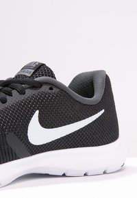 Černá a šedá běžecká obuv Nike s bílým znakem Swoosh a bílou podrážkou, zobrazující detaily boční strany a paty na jednoduchém pozadí.