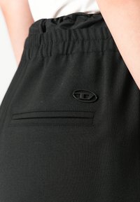 Elastický pás na čiernych nohaviciach s malým čiernym oválnym logom nad horizontálnou zadnou vreckom.