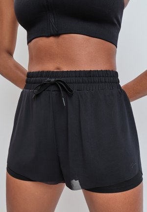 Gros plan d'une personne portant un short de sport noir à plusieurs couches avec une taille élastique et un soutien-gorge de sport noir.