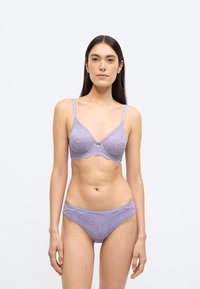 Levandų nėrinių liemenėlė ir atitinkantis apatinis trikotažas, puoštas gėlių raštais, reguliuojamomis petnešėlėmis ir banguotomis kraštinėmis, užtikrinančiomis tobulą užbaigtumą.