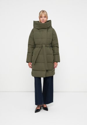Olijfgroene pufferjas met een hoge kraag, een ceintuur in de taille en een gewatteerd patroon, gecombineerd met wijde donkerdenim broek en zwarte schoenen.