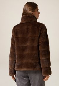 Braune Felljacke mit hohem Kragen, die ein horizontal gestreiftes Muster und lange Ärmel hat. Die Textur ist weich und dicht.