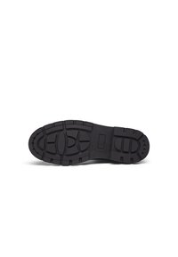 Black rubber shoe sole featuring a patterned tread for grip, showcasing various shapes and textures for enhanced traction and durability.