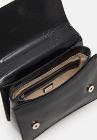 Černá kabelka z umělé kůže s krokodýlím vzorem, béžovou podšívkou a dvěma vnitřními kapsami. Zapínání na druky.