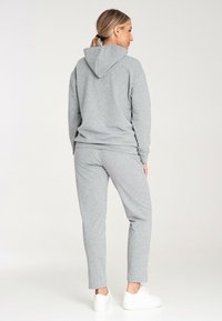 Szary sweter z kapturem oraz pasujące dresy z miękkiej, teksturowanej tkaniny. Charakteryzuje się kapturem, elastycznym pasem w talii i dopasowanymi mankietami. Białe sneakersy dopełniają całość.