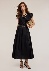 Blusa nera con spalle volanti, dettagli ricamati; gonna nera a vita alta; tacchi neri con cinturini; borsa dorata; collana nera a strati.