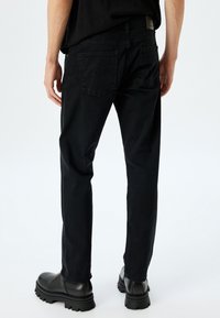 Pantalones de mezclilla negros con un ajuste recto, que cuentan con dos bolsillos traseros y una cinturilla lisa. Textura suave con un ligero brillo.