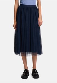 Gonna midi in tulle blu navy con pieghe a strati, vita elasticizzata e sovrapposizione trasparente. Abbinata a mocassini neri in vernice.