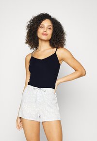 Zwarte mouwloze top gecombineerd met lichtblauwe shorts met een subtiel abstract patroon en een verstelbare trekkoord taille.