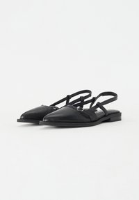 Schwarze Leder-Slingback-Schuhe mit spitzem Zeh, flachem Absatz und zwei dünnen verstellbaren Riemen mit einem kreisförmigen silbernen Akzent.