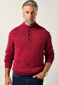 Roter strukturierten Strickpullover mit hohem Kragen, ausgestattet mit einer Knopfleiste und gerippten Bündchen. Wird mit dunklen Jeans getragen.